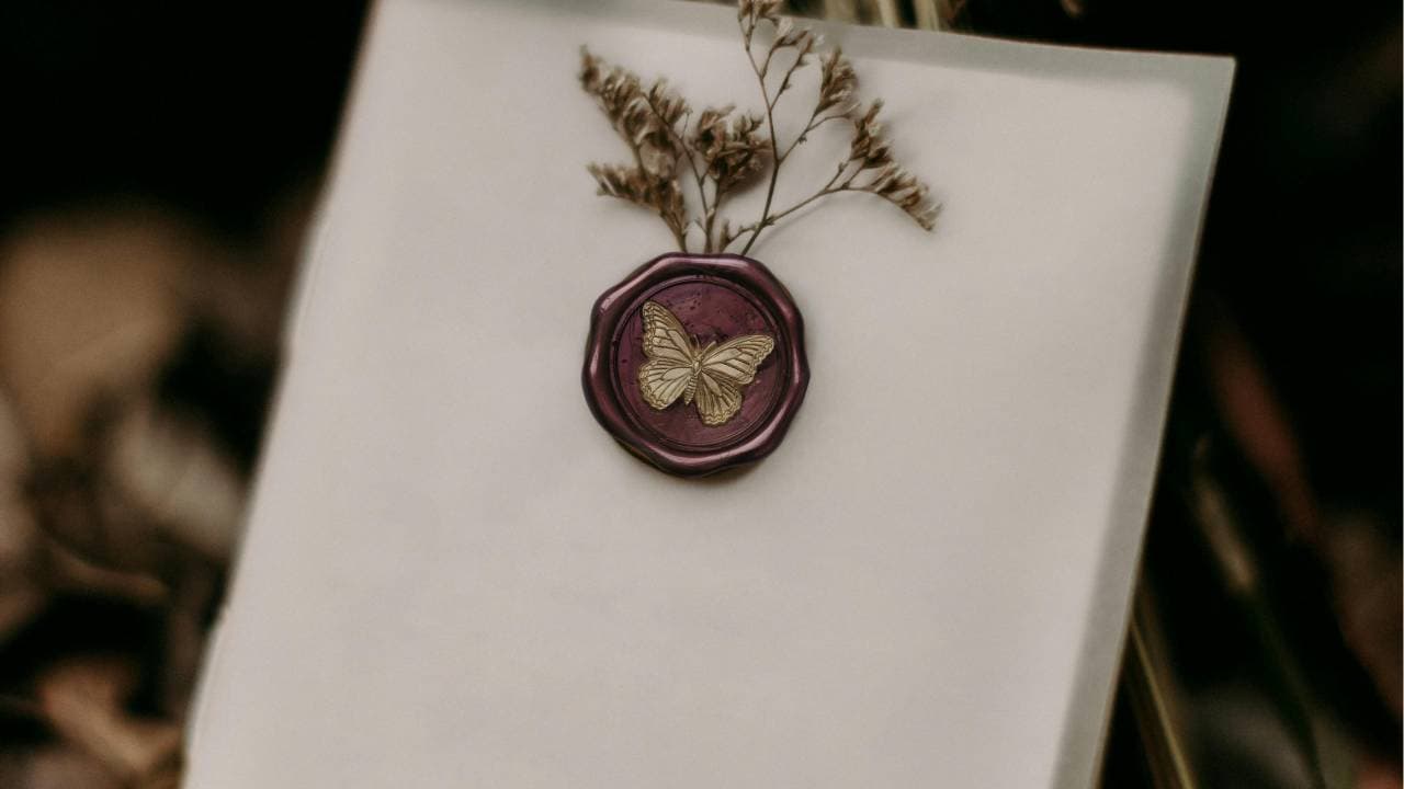 A blank sheet of paper with a purple wax seal featuring a butterfly and a dried flower arrangement.