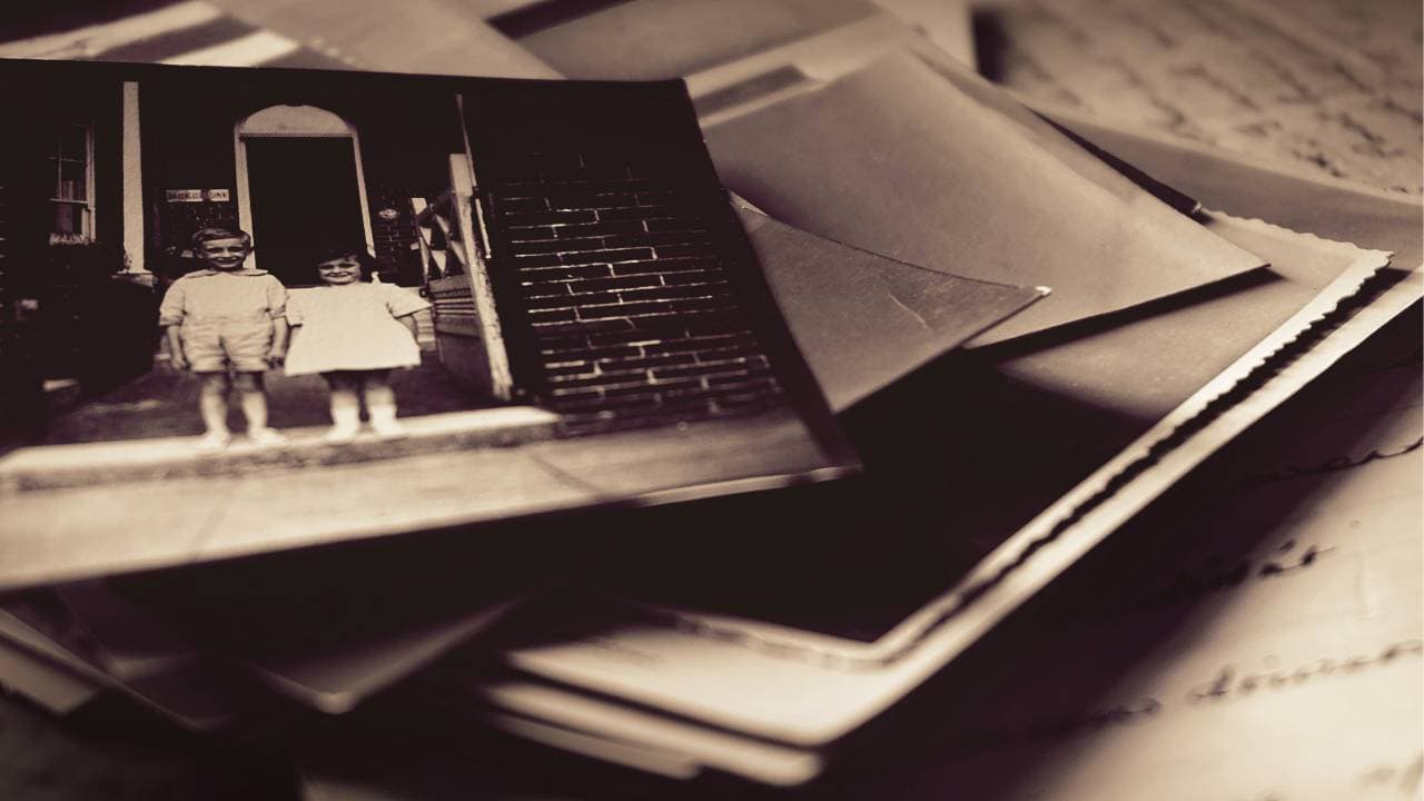 Two children stand on a porch, surrounded by scattered old photographs and letters.